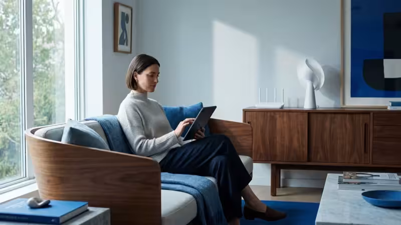 A homeowner using a tablet in a modern smart home living room with a router visible.