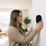 Homeowner adjusting a smart thermostat in a bright, modern living room.