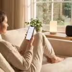 A woman using a smartphone to control devices in a bright, modern smart home with minimalist decor.