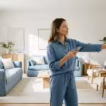 A person using a smartphone to control a smart thermostat in a bright, modern living room.
