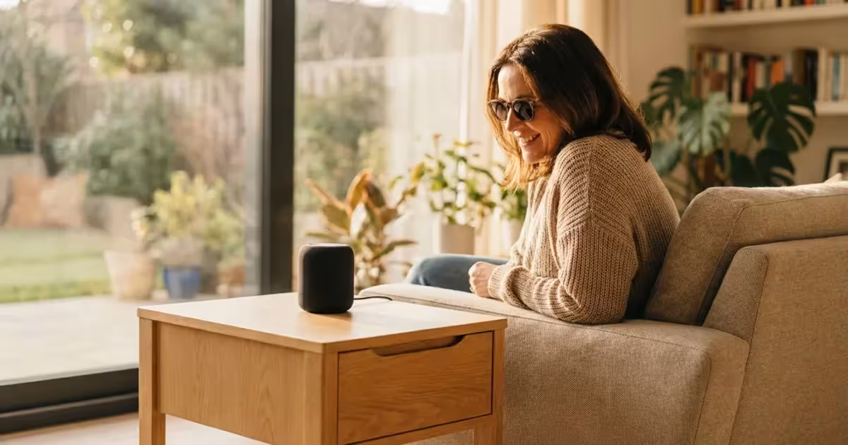 A visually impaired woman smiling while interacting with a smart speaker in a bright, modern living room.
