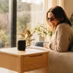 A visually impaired woman smiling while interacting with a smart speaker in a bright, modern living room.