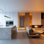 A modern home interior showing a transition from cool daylight kitchen lighting to warm amber living room lighting.
