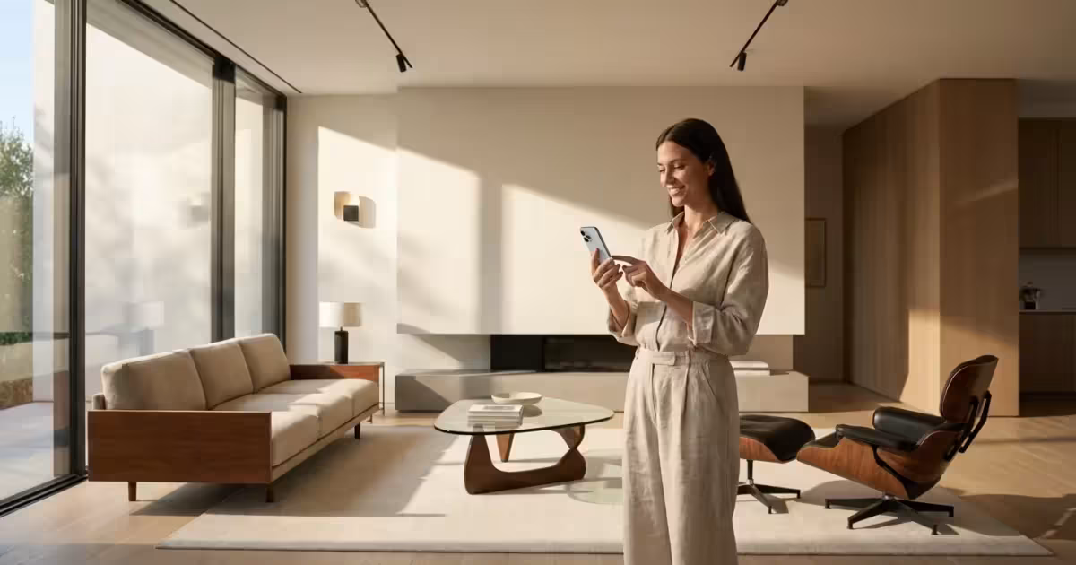 A woman using a smartphone to control the lighting in a bright, modern minimalist living room.