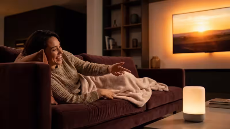 A person comfortably using voice commands to control their TV in a cozy, modern living room.